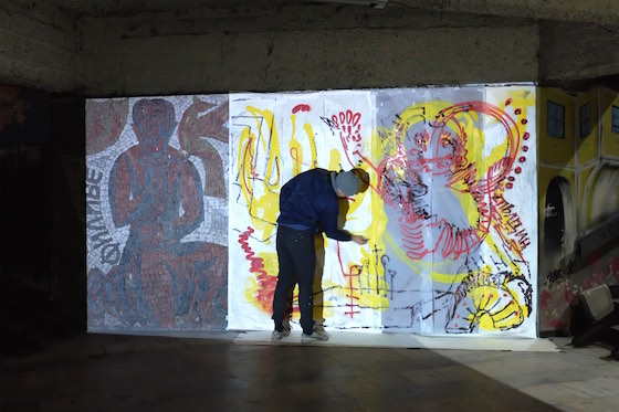 two artist paint live on a wall and trace cave paintings